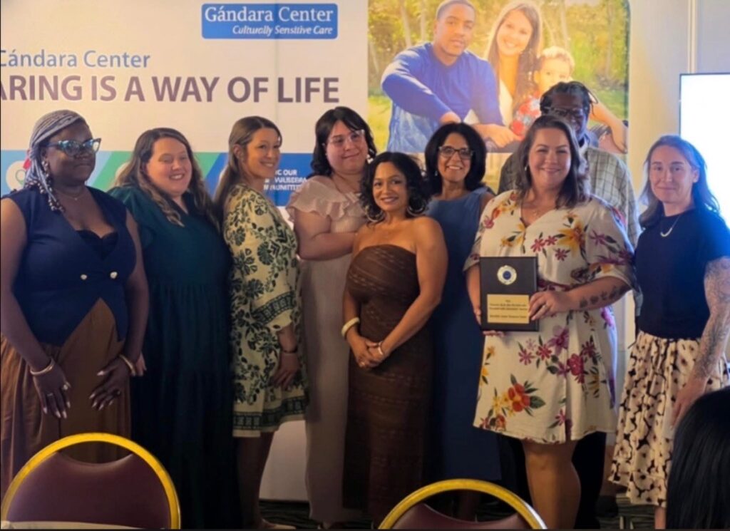 Members of the Westfield Family Resource Center team pose together at the Gándara Center Annual Staff Recognition Event, in front of a banner reading "Caring Is a Way of Life." One team member holds the Program of the Year award plaque.